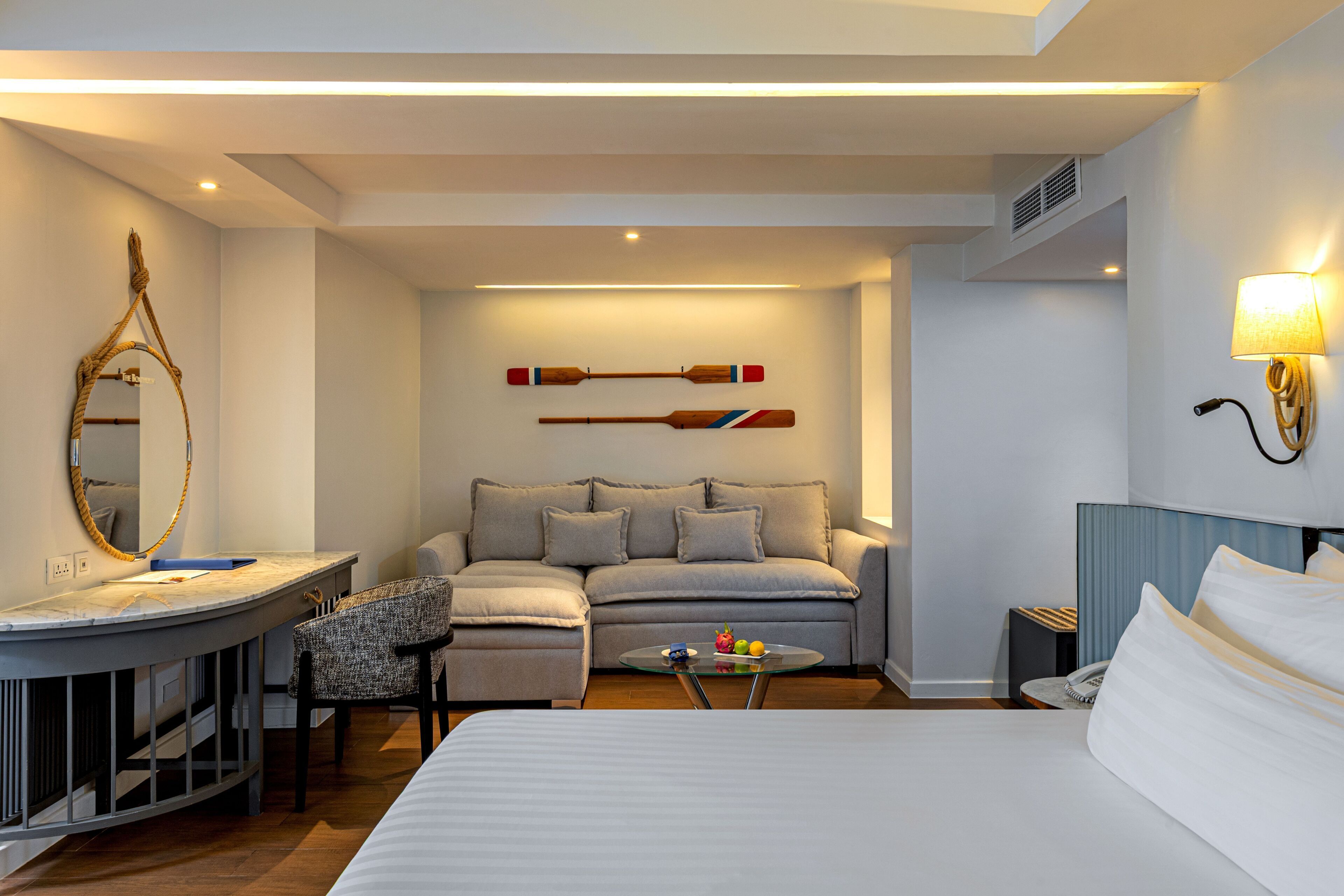 Habitación de hotel con cama, sofá, una mesita, un espejo y dos tablas de paddle fijadas a la pared.