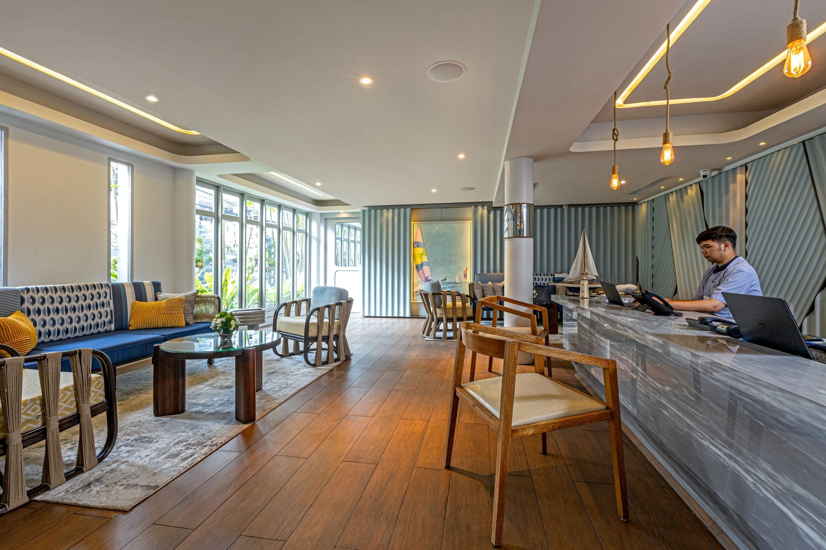 Un hall d’hôtel moderne avec un comptoir d’accueil, un espace salon et de grandes fenêtres.