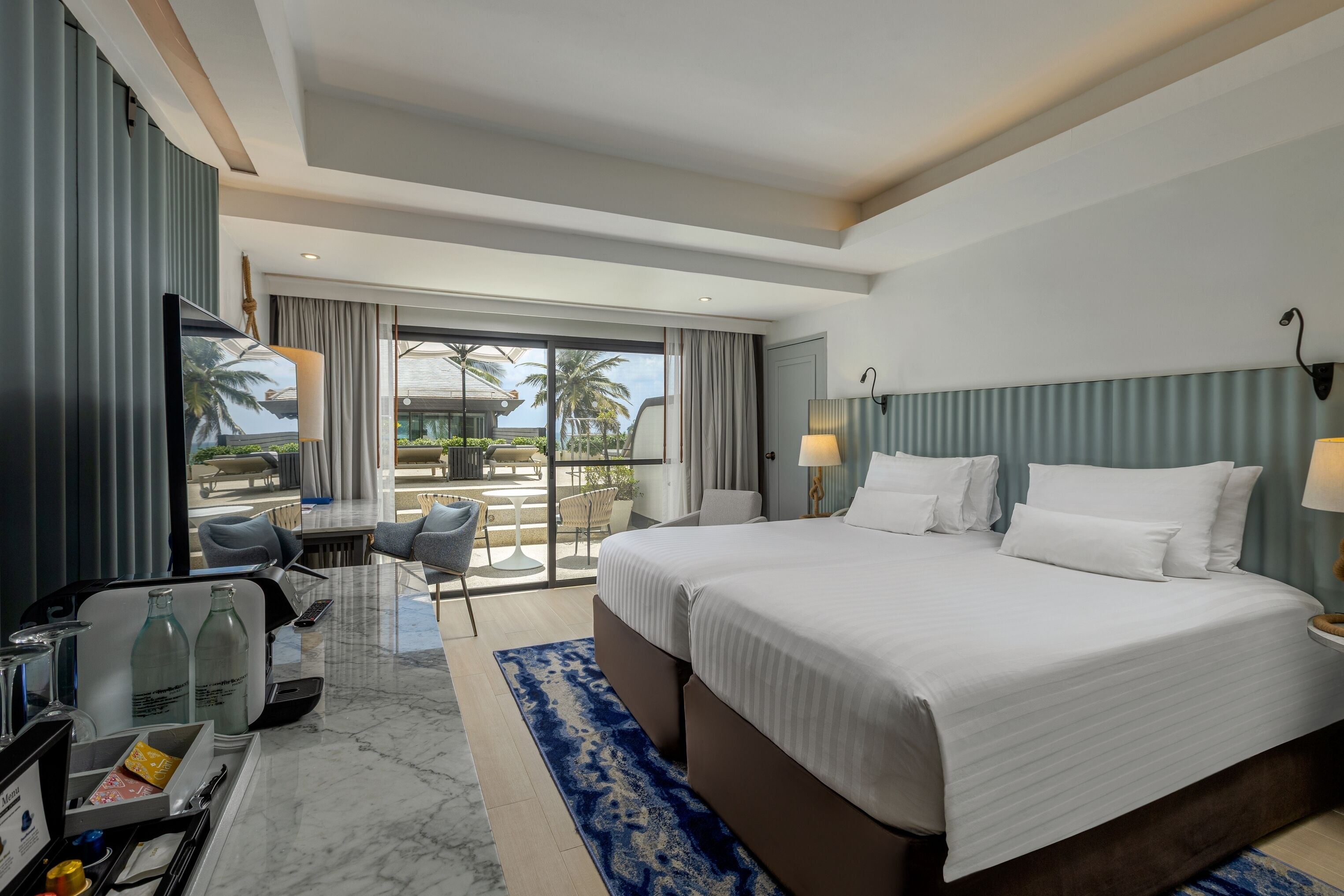 A hotel room with a large bed, a desk with a computer, a chair, and a view of a pool and palm trees.