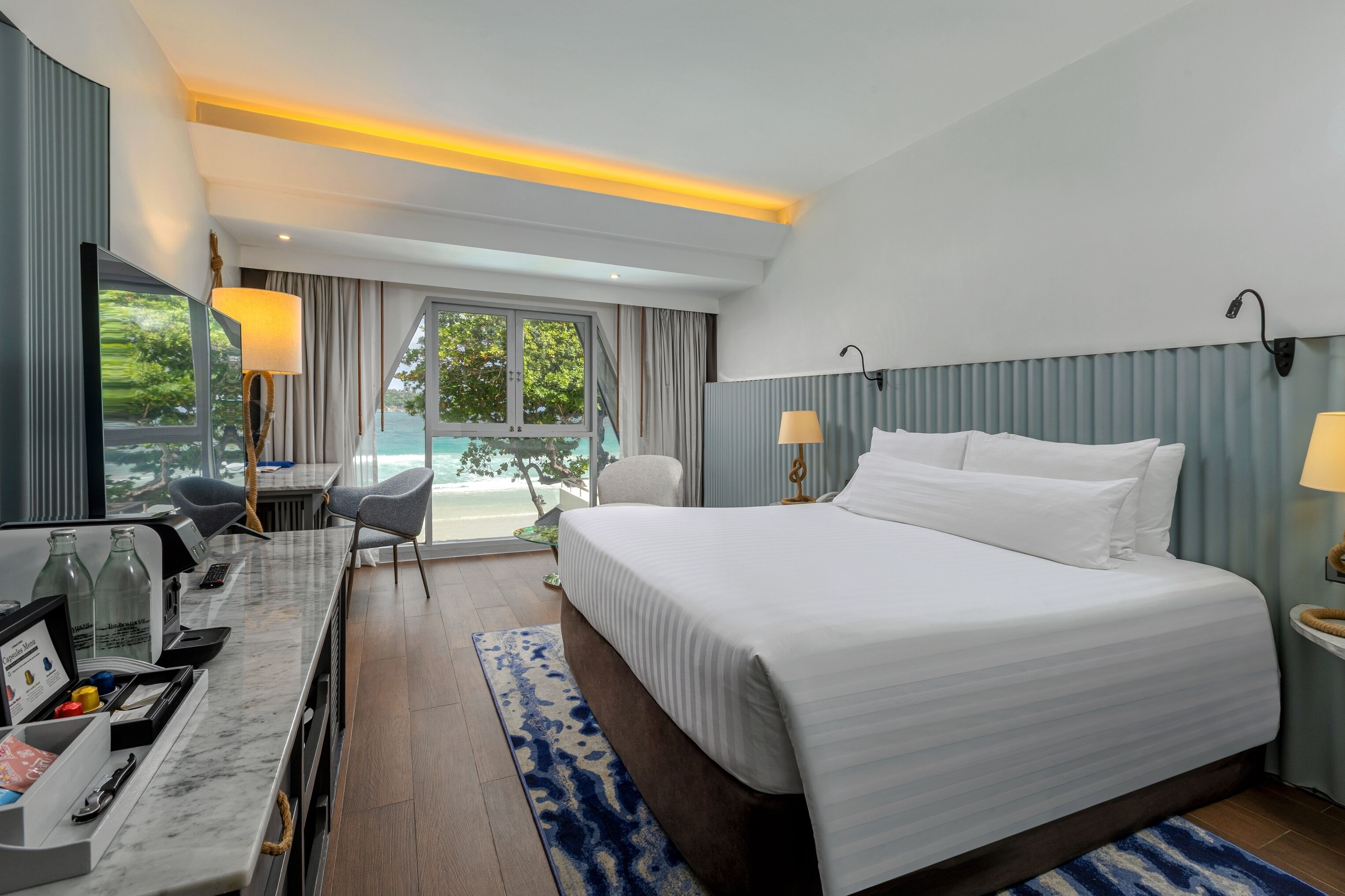 A hotel room with a bed, a desk with a computer, a chair, and a view of the ocean.
