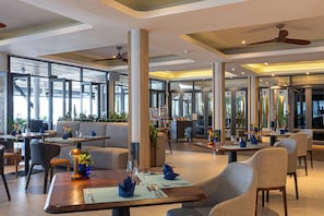 A modern restaurant interior with high ceilings, large windows, and a variety of seating options including tables and booths. - The Boathouse Phuket (Karon)