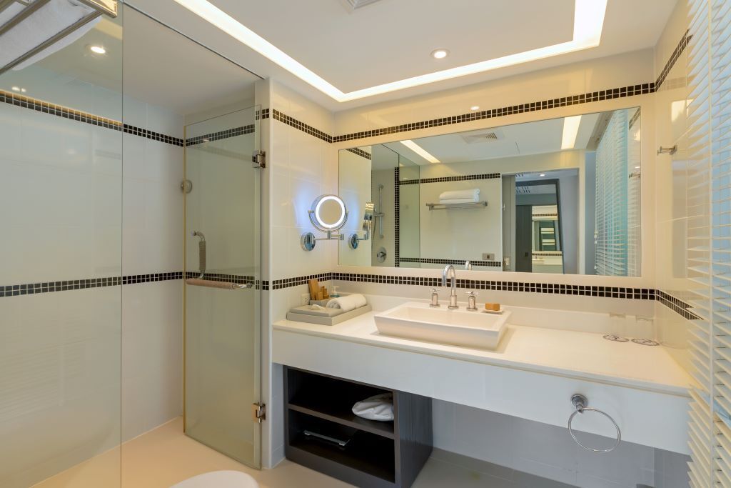 A modern bathroom with a glass shower enclosure, a large mirror, and a white sink with a towel rack.