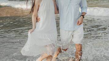 Una pareja caminando por aguas poco profundas en una playa con una costa rocosa al fondo.