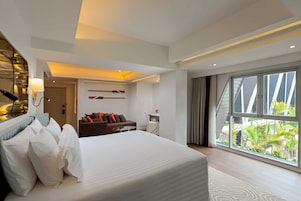 Habitación de hotel moderna con una cama grande, un escritorio, una silla y vistas al exterior a través de amplias ventanas.
