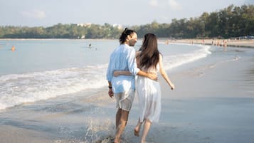 Una pareja caminando en una playa con olas y una costa lejana.