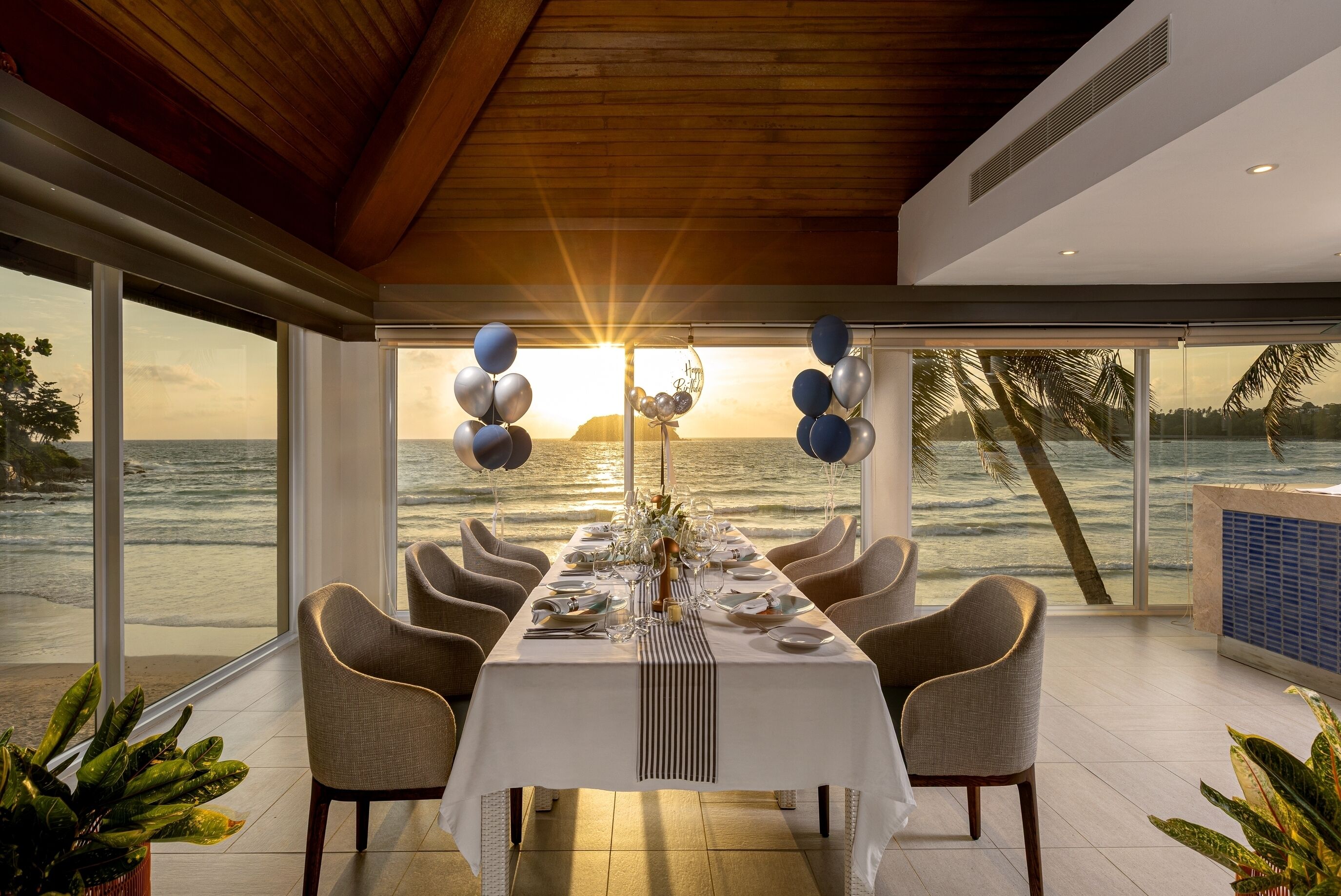 A dining area with a view of the ocean, a table set for a meal, and balloons.