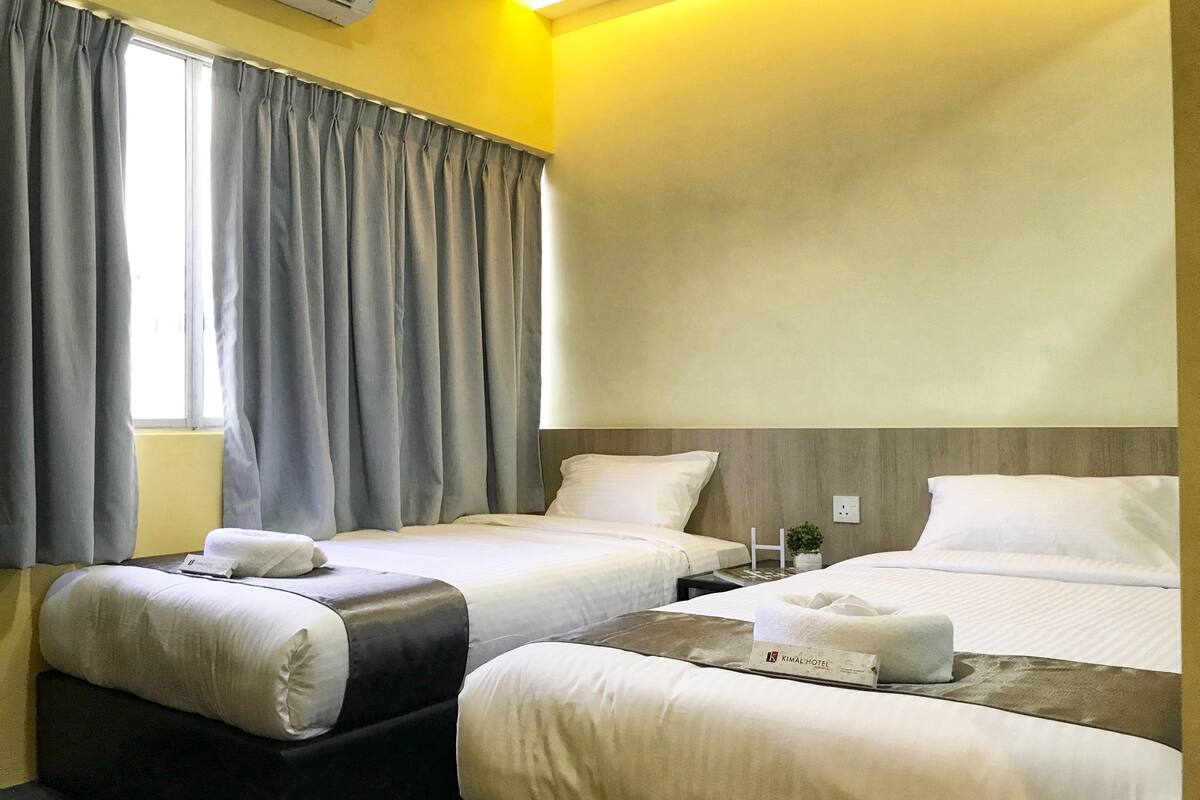 A hotel room with two beds, a small table, a sofa, and a window with curtains.