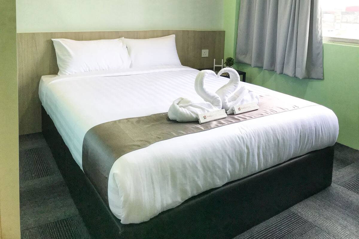 A hotel room with a bed, pillows, a blanket, and a towel arrangement.