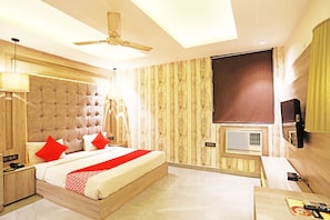 A modern hotel room with a large bed, a ceiling fan, a flat-screen TV, and a window with blinds. - OYO 8902 Hotel Ronald Inn (Faridabad)