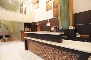 A reception area with a marble floor, a reception desk, a clock, and a staircase in the background. - OYO 8902 Hotel Ronald Inn (Faridabad)