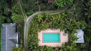Vue aérienne d’un complexe hôtelier doté d’une piscine centrale, entouré d’une végétation tropicale luxuriante et de plusieurs bâtiments.