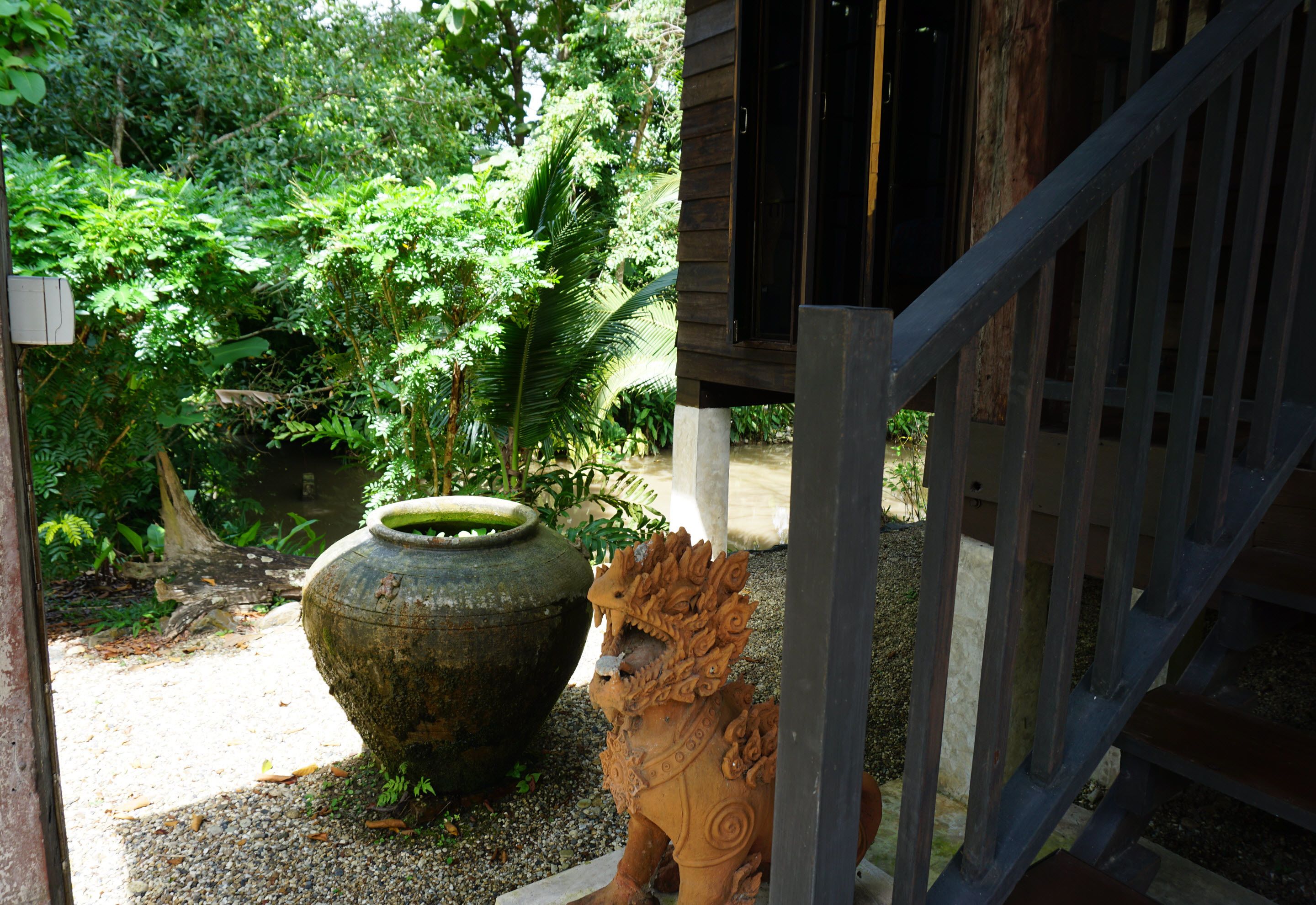 A rustic wooden structure with a lion statue in front, surrounded by lush greenery and a large planter.