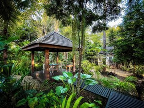 A wooden gazebo with a tiled roof surrounded by lush greenery and a small table with chairs. - Mae Nai Gardens (Mae Rim)