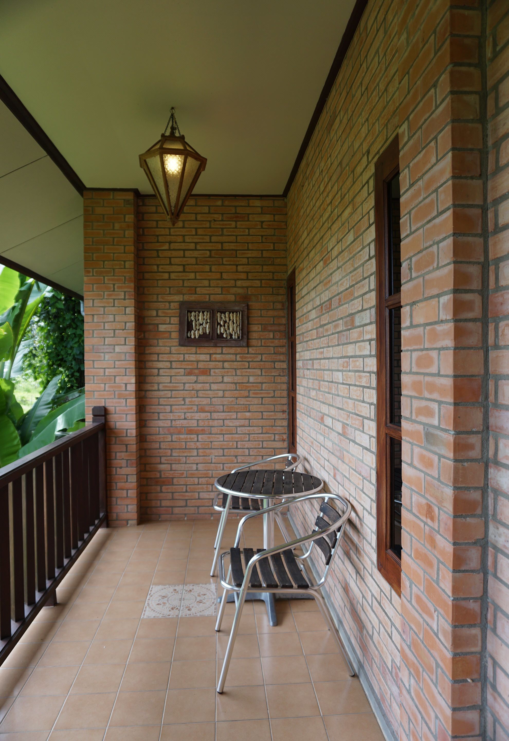 A brick-walled balcony with a tiled floor, a metal table with chairs, and a hanging lantern.