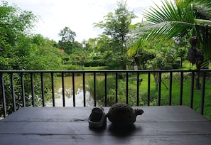 A wooden deck with two ceramic objects, overlooking a lush garden and a pond. - Mae Nai Gardens (Mae Rim)