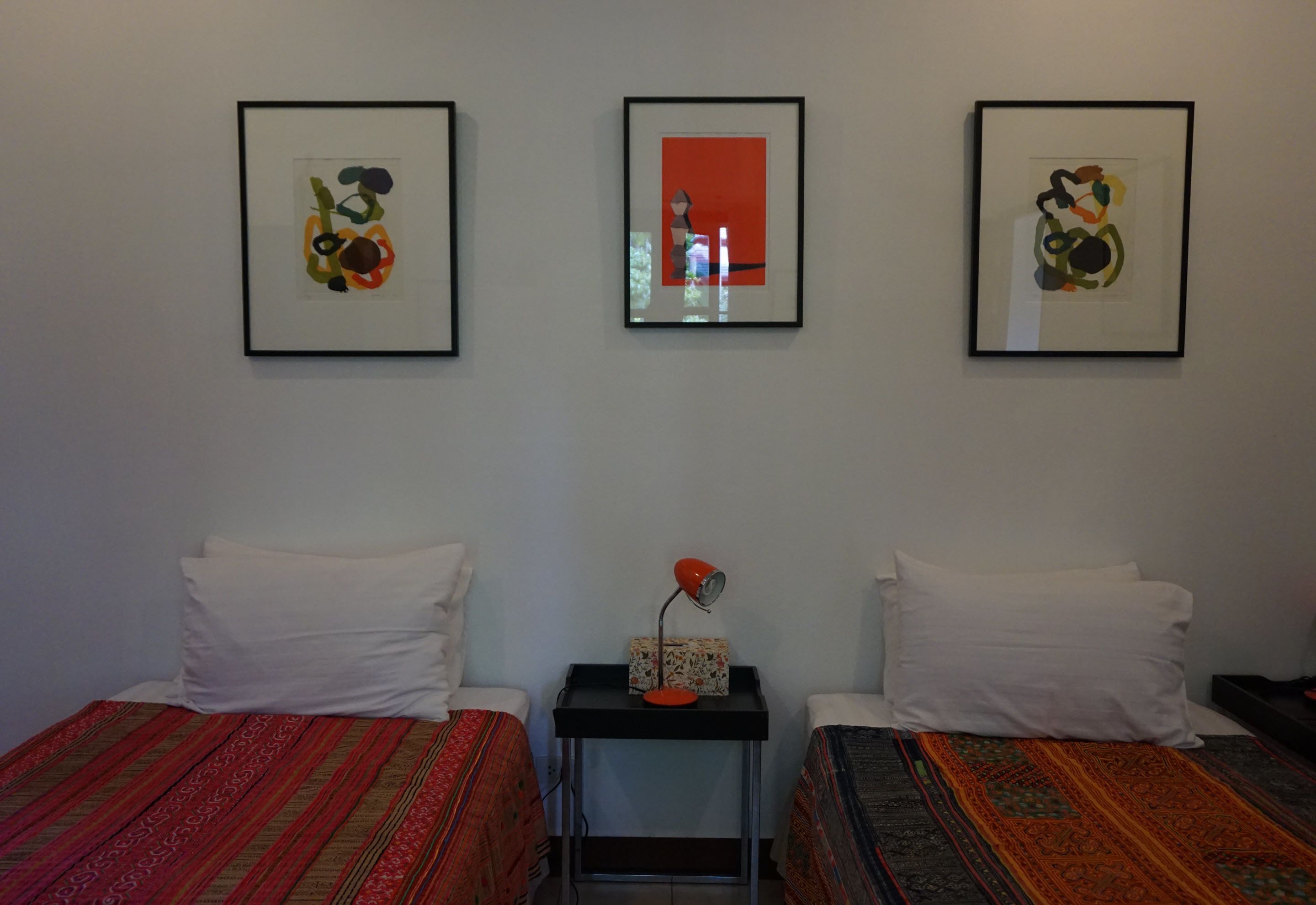 Une chambre avec deux lits, chacun agrémenté d’une literie à motifs, une petite table avec une lampe et trois œuvres d’art encadrées accrochées au mur.
