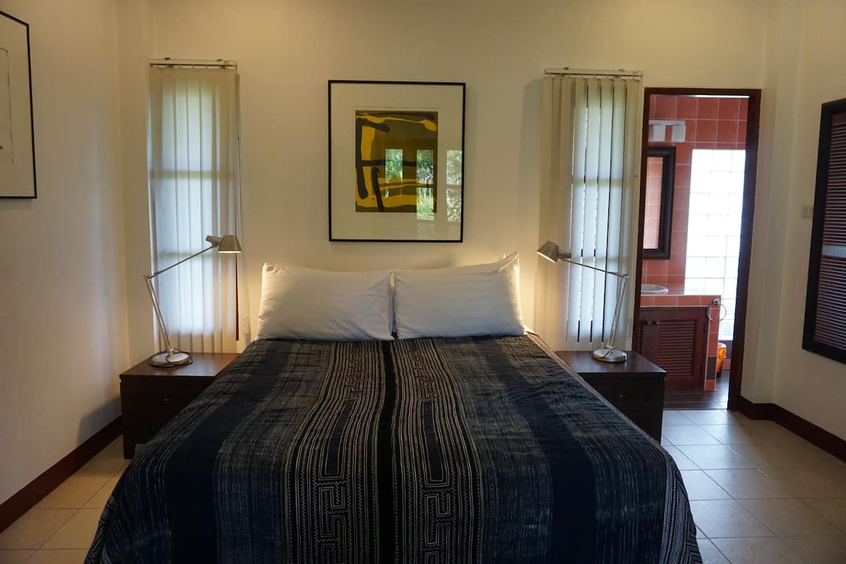 A hotel room with a large bed, two bedside tables, a framed artwork above the bed, and a view of the bathroom through a door.