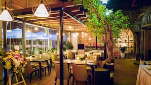 An indoor dining area with tables and chairs, a large tree, and hanging lights.