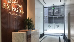A reception area with a wooden wall displaying 'LEXINGTON APARTMENTS' sign, a reception desk, and a potted plant.