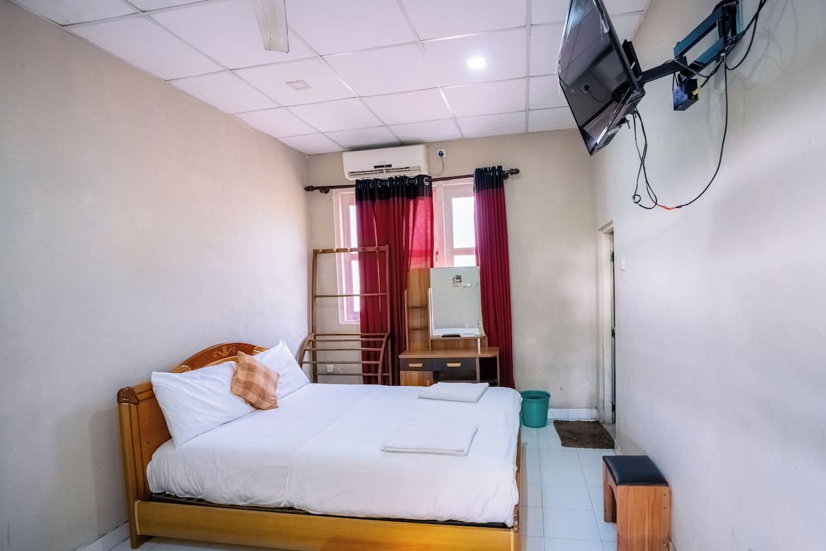 A small, neatly arranged bedroom with a single bed, a desk, and a TV mounted on the wall.