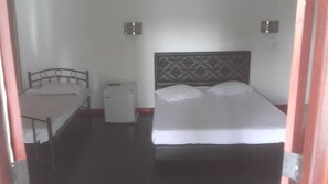 A small, single-room hotel room with a bed, a nightstand, a small table, and a wall-mounted heater. - The Kingston hotel (Kiribathgoda)