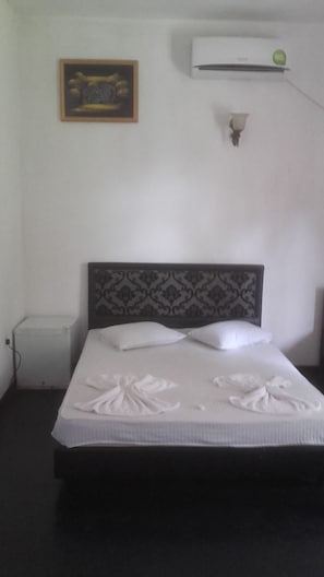A neatly made bed with a patterned headboard, a small bedside table, and a wall-mounted air conditioner. - The Kingston hotel (Kiribathgoda)