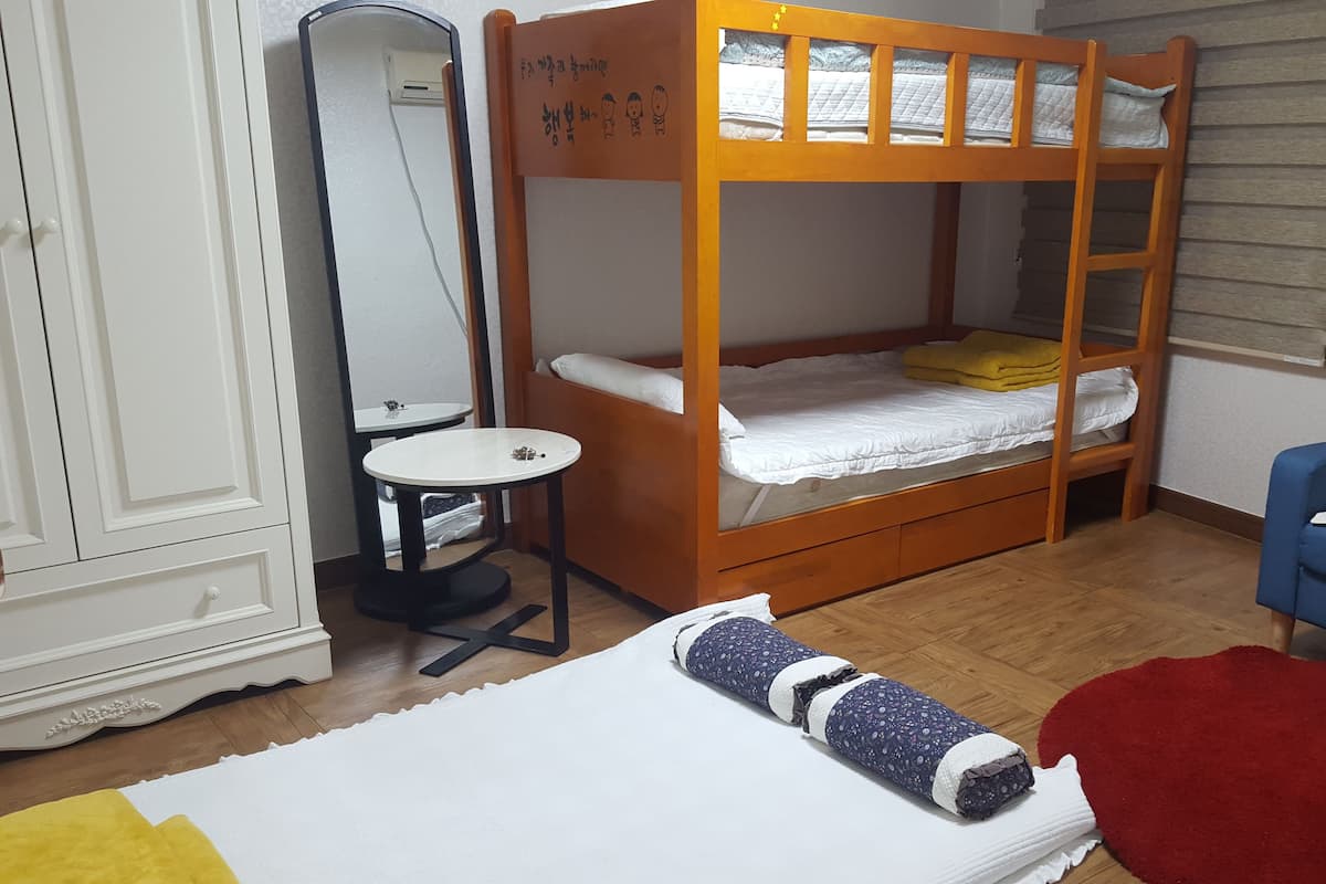 Een stapelbed met een klein tafeltje en stoel, een spiegel en een rood vloerkleed in een kamer met houten vloer.