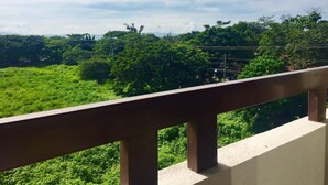Un balcón con vista a un paisaje verde exuberante y árboles distantes bajo un cielo parcialmente nublado.