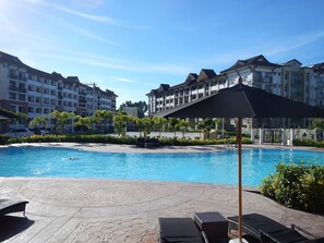 A swimming pool with lounge chairs and umbrellas, surrounded by multi-story buildings with balconies.