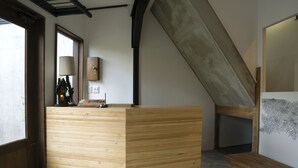 Ein hölzerner Empfangstresen in einem modernen Raum mit schrägverdeckter Decke, einem Fenster und einer Wandlampe.
