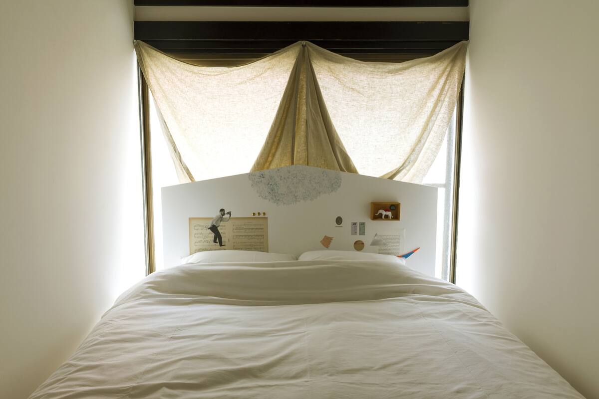 A neatly made bed with a headboard that has a bulletin board and a small shelf.