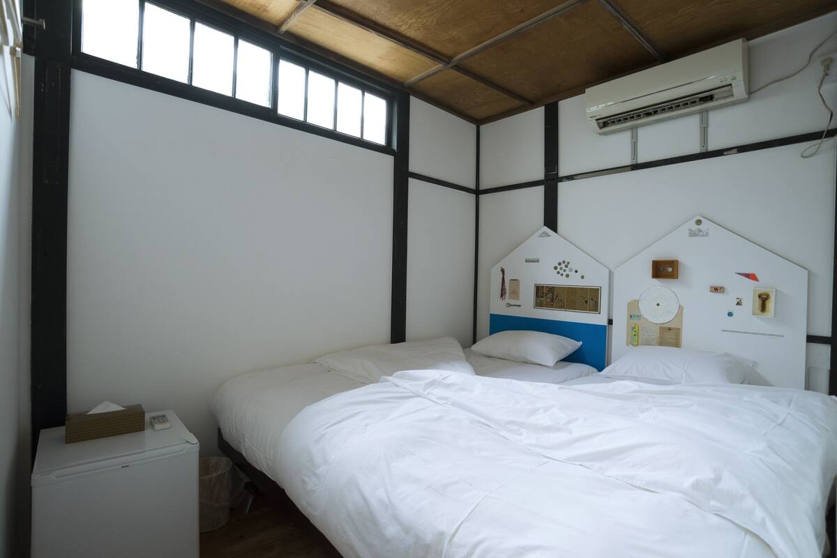 A bedroom with a bed, a small bedside table, an air conditioning unit, and a window.