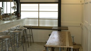Ein Restaurantinneres mit einem langen Holztisch, Metallhockern und einer modernen Kronleuchter.