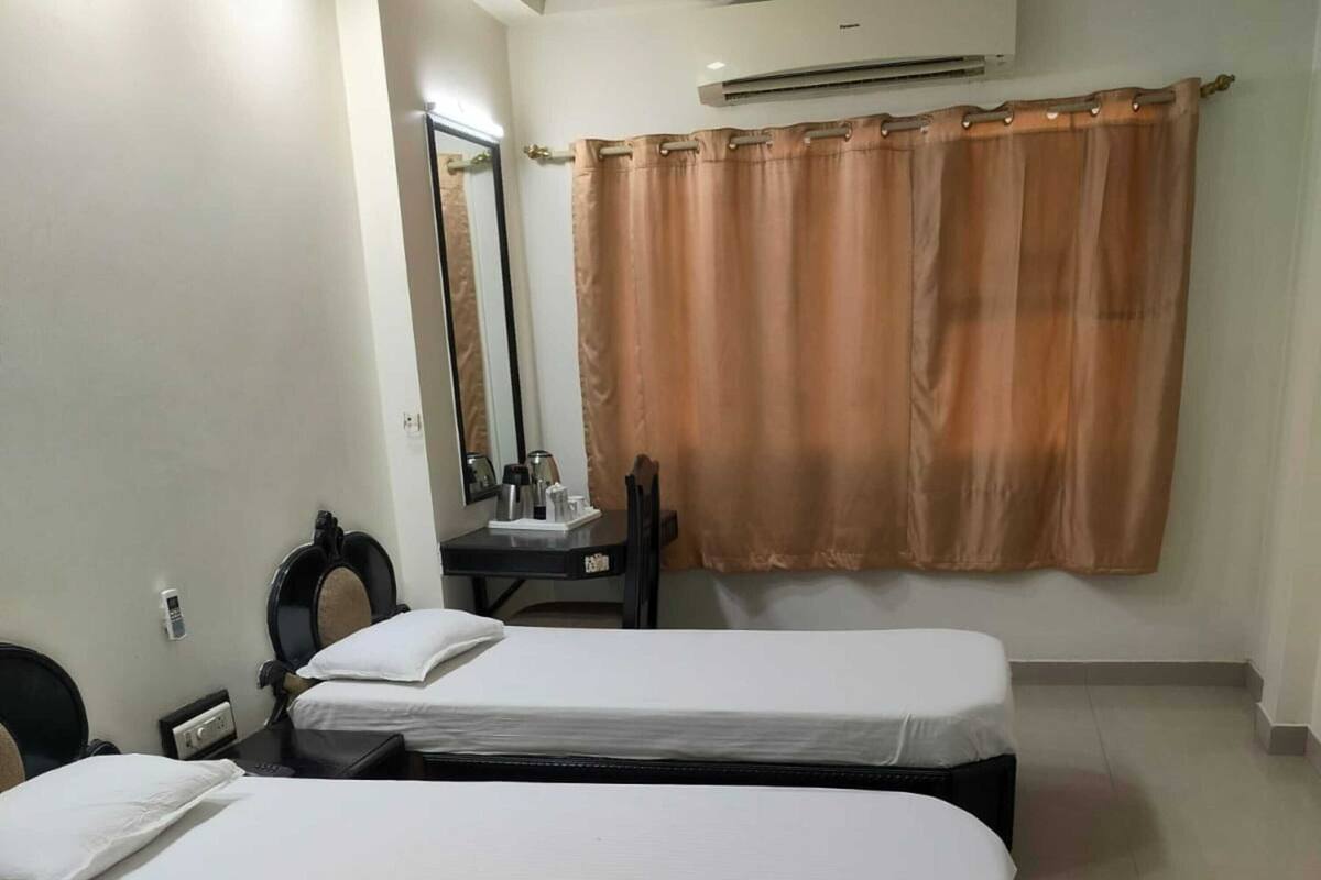 A hotel room with two single beds, a desk with a chair, a small table with a red cup, and a large mirror.