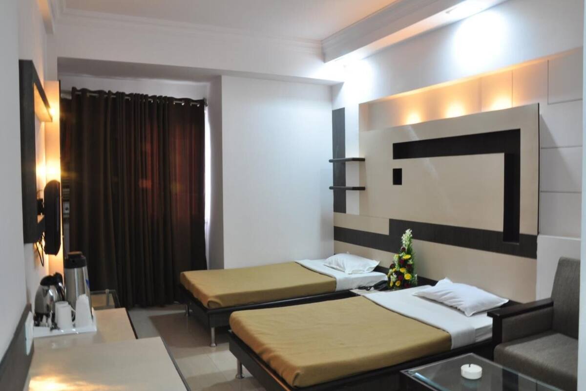A hotel room with two single beds, a sofa, a glass coffee table, a TV, and a wall-mounted shelf.
