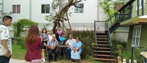 A group of people seated around a table in a courtyard with a staircase and greenery.