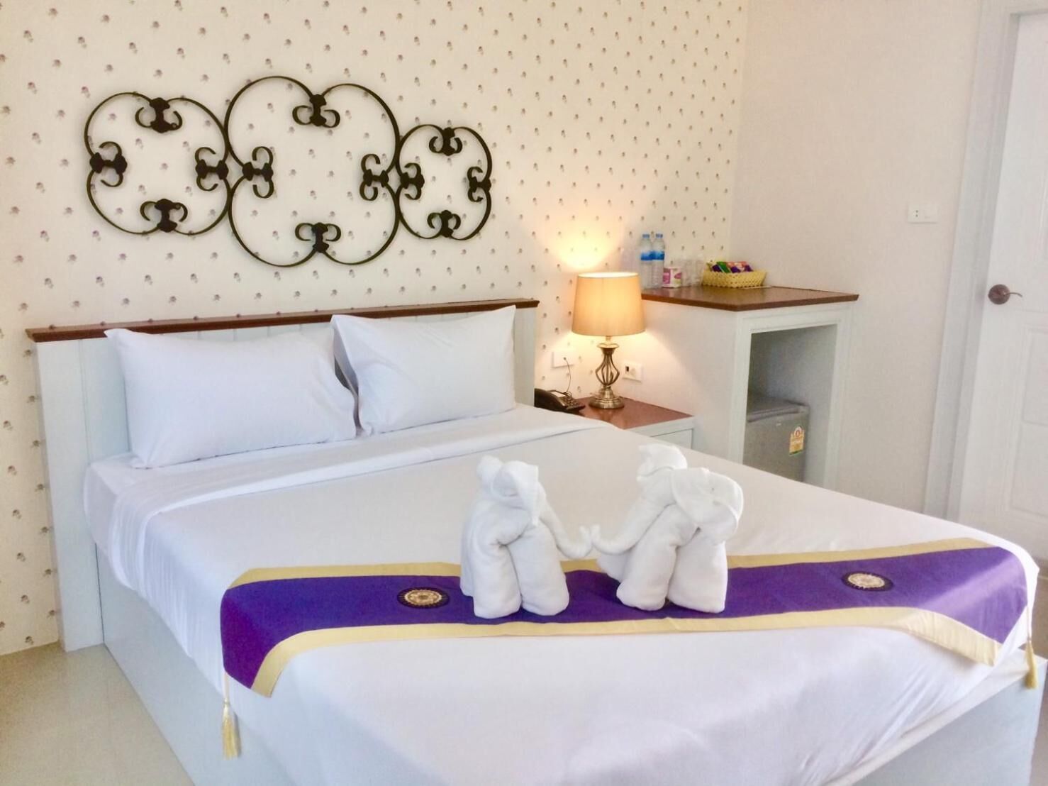 Een net opgemaakt bed met witte lakens, een paars en goud beddegoed en twee witte handdoeken op het bed.
