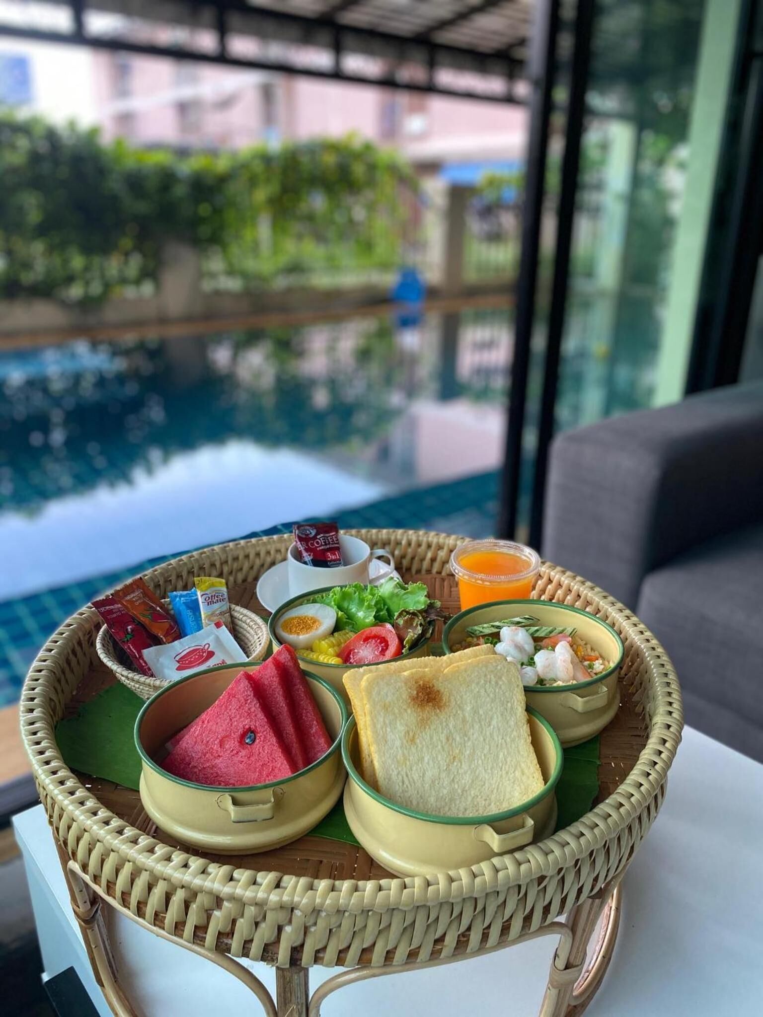 A breakfast tray with various food items and a cup of coffee on a table near a pool.