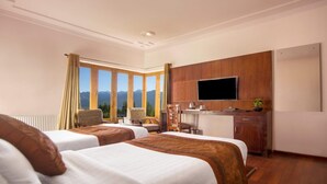 A hotel room with two beds, a desk, a TV, and a view of mountains.