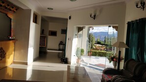 A hotel lobby with a reception desk, a seating area with a sofa and armchairs, and a view of the mountains through a glass door.