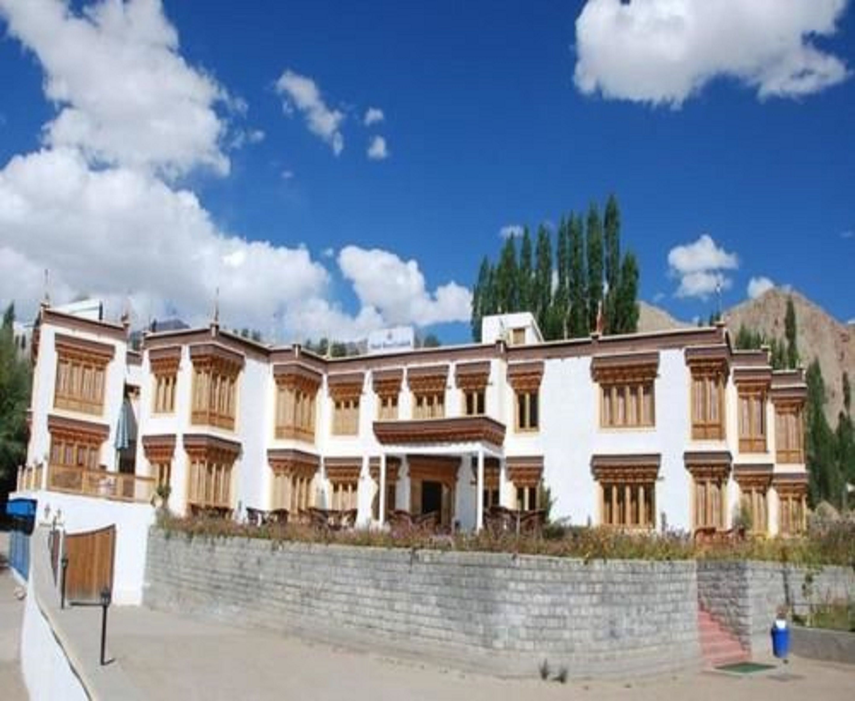 A multi-story building with traditional architectural style, featuring balconies and a stone wall in front.