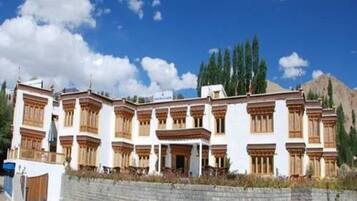 A multi-story building with traditional architectural style, featuring balconies and a stone wall in front.