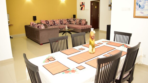 A dining area with a table set for six, surrounded by chairs, and a sofa in the background.