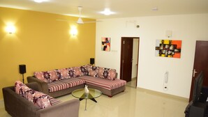 A living room with a sectional sofa, a glass coffee table, and a television.