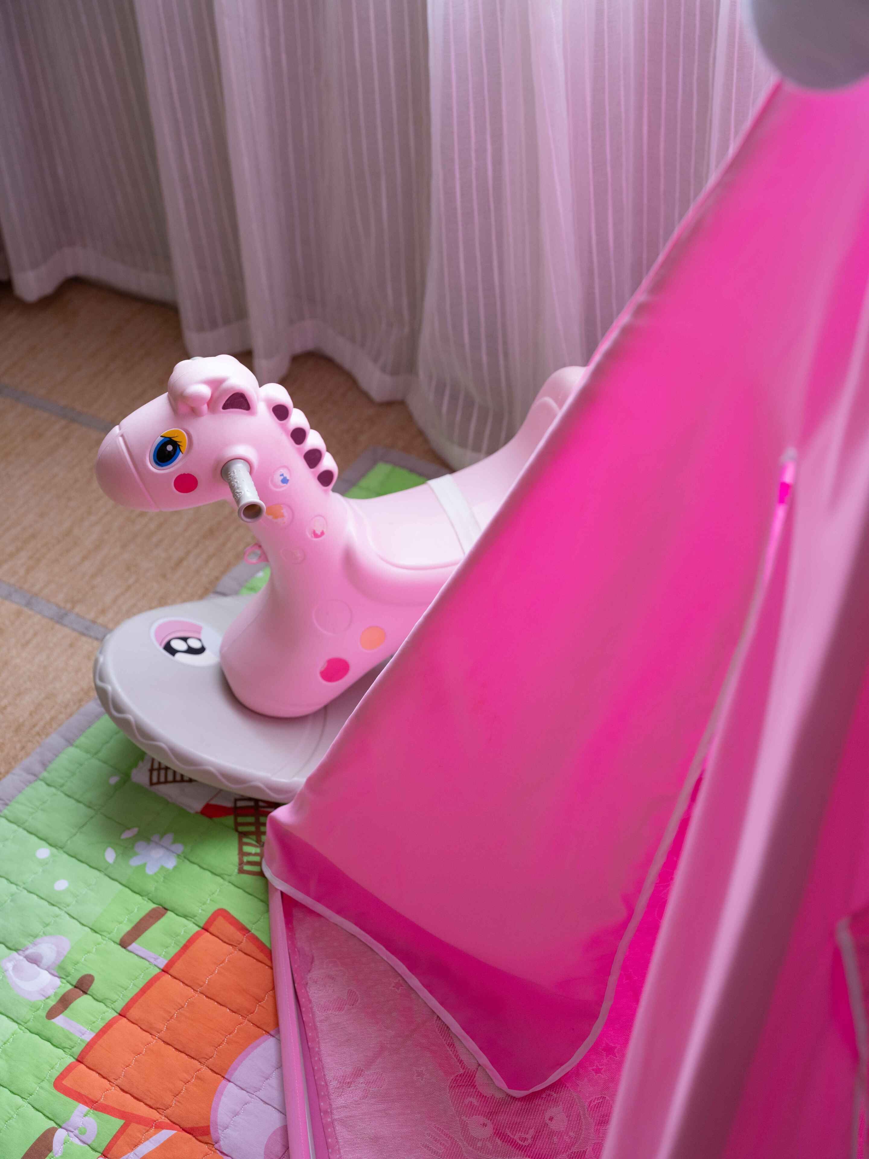 A pink toy giraffe on a white chair with a green and orange patterned rug.