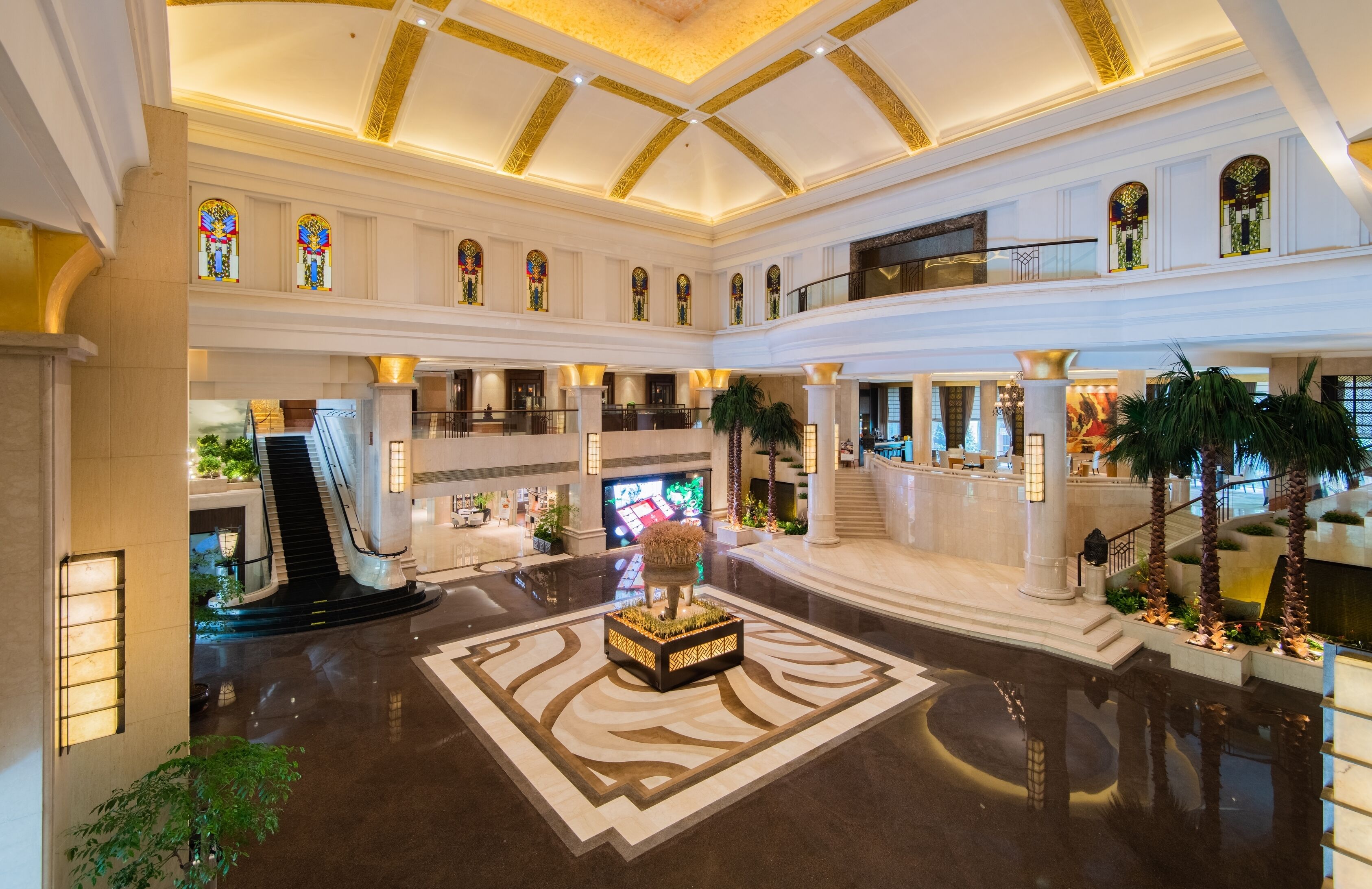 Un vestíbulo amplio con una fuente central, varias escaleras y un techo alto con diseños decorativos.