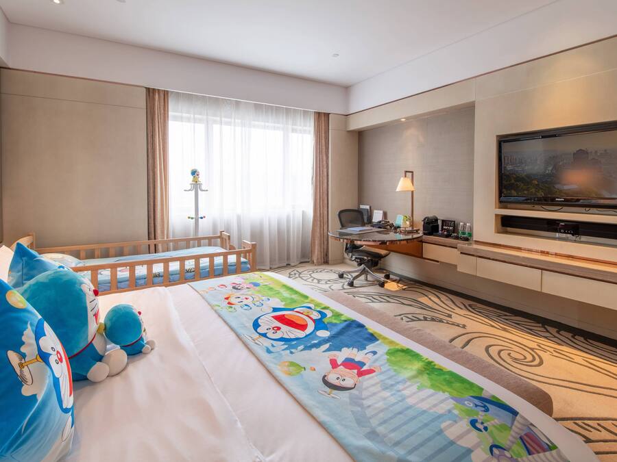 A hotel room with a bed, a desk, a chair, a TV, and a window with curtains.