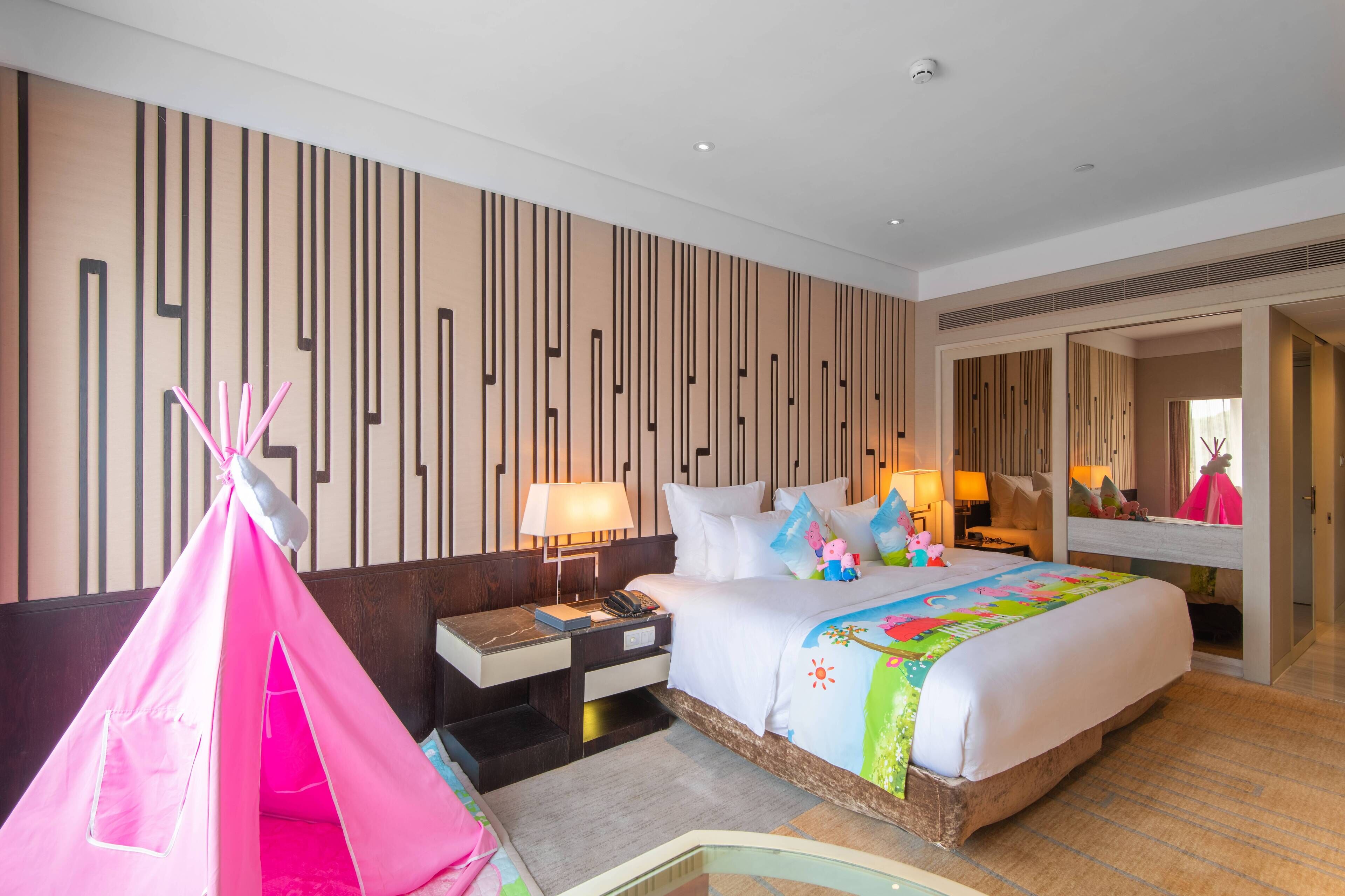 Quarto de hotel com cama, mesa de cabeceira, abajur, uma tenda rosa e um espelho.