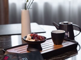 Una bandeja con un cuenco de frutas secas y nueces, dos tazas negras y una tetera negra sobre una mesa de madera.