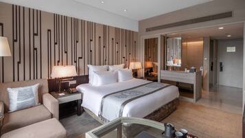 A modern hotel room with a large bed, a sofa, a desk, and a bathroom visible through an open door.